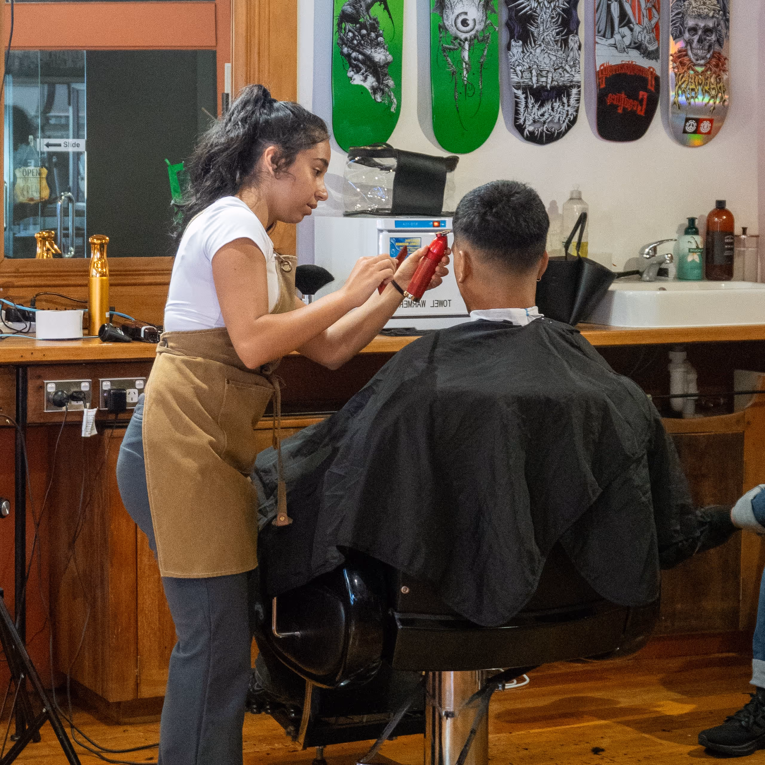 A modern barber shop interior featuring two brown leather barber chairs, a small side table, and large windows allowing natural light, with a comfortable couch in the corner.